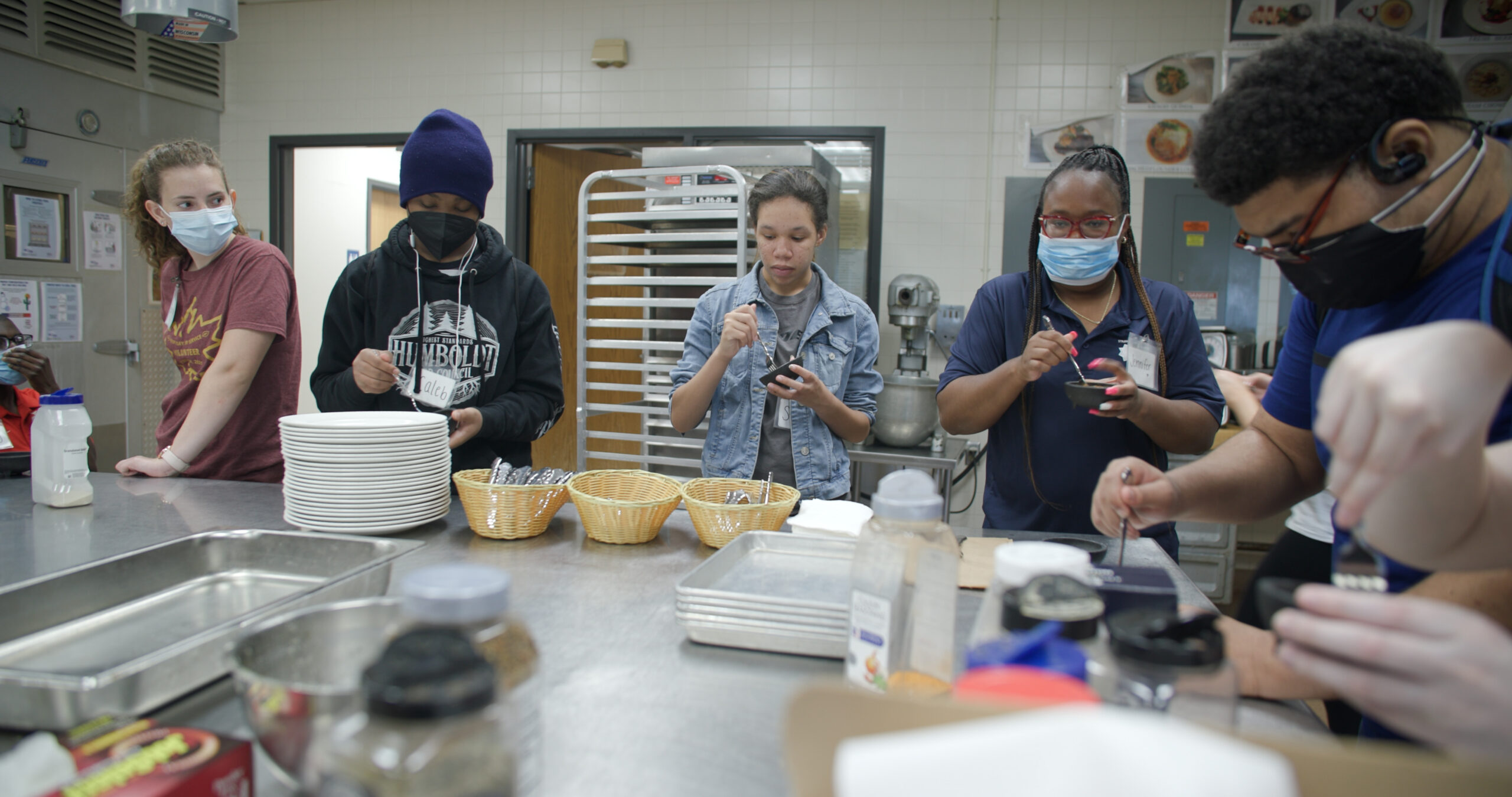 Several students mix ingredients in small bowls in a commercial kitchen